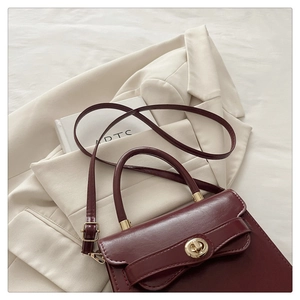 Detail of a deep red square handbag with a gold twist lock and a sleek leather texture