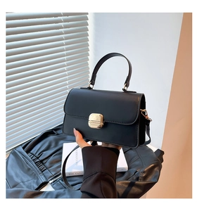 Detailed view of black matte leather handbag with gold square buckle and detachable strap