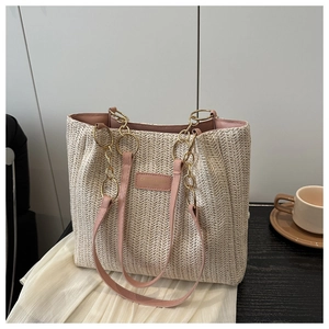 Detail of woven straw tote bag featuring pink leather straps and gold metal chain links