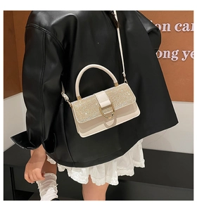 Detail of rhinestone flap and golden U-shaped buckle on an elegant cream mini crossbody bag