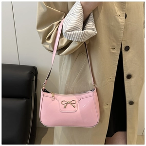 Pink patent leather underarm bag with golden metal bow detail shown on a model