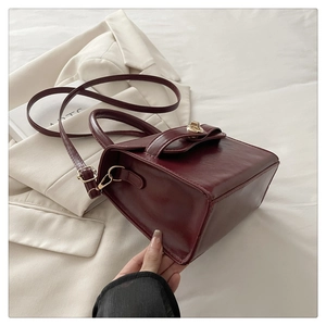 Detail of burgundy leather handbag with gold twist lock and handle in hand