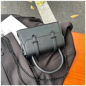 Détail d'un sac en cuir saffiano noir avec chaîne en métal sur fond de blazer chic