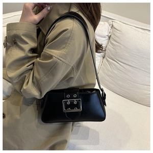 Detail of a black glossy leather shoulder bag with silver buckle worn with a beige coat