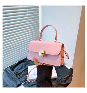 Detail of pink leather handbag with gold twist lock and crossbody strap held by hand