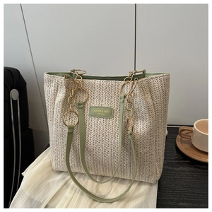 Detail of woven straw tote bag featuring green leather trim and gold chain shoulder strap