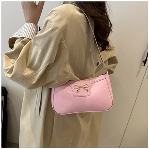 Close-up of pink patent leather baguette bag with a gold metal bow on a shoulder strap