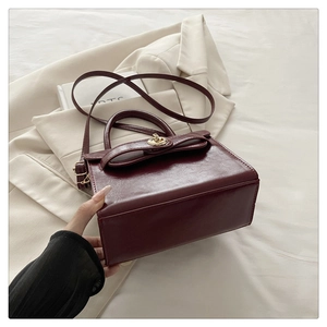 Detail of burgundy handbag with bow flap design and golden rotating metal lock closure