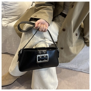Detail of black rectangular underarm bag with silver buckle worn by a model in a trench coat