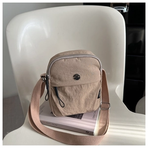 Detail view of khaki nylon crossbody bag with adjustable strap on a white chair
