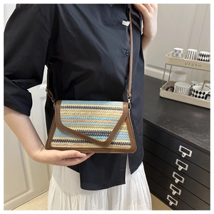 Detail shot of a colorful woven straw crossbody bag with brown faux leather trim and strap