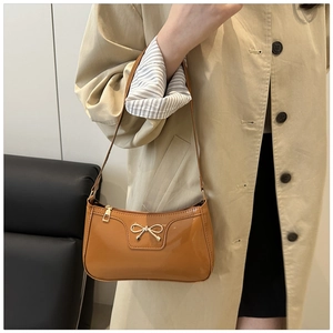 Detail of glossy patent leather shoulder bag with a gold bow buckle on a baguette bag