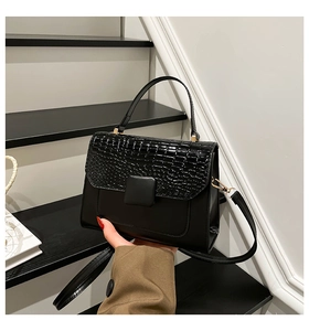 Detail of black faux crocodile texture flap on a minimalist crossbody square handbag