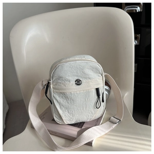Detail of white nylon crossbody bag featuring a branded metal buckle and zippered pocket