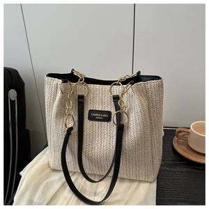 Detail of herringbone weave straw tote bag with black leather straps and gold chain link