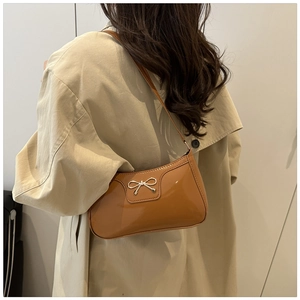 Detail of glossy brown lacquer shoulder bag with gold bow clasp and elegant beige trench coat