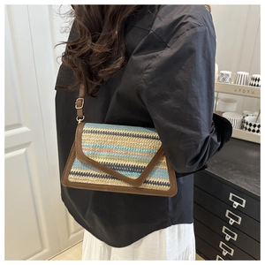 Model wearing a striped woven straw crossbody bag with brown leather trim and flap