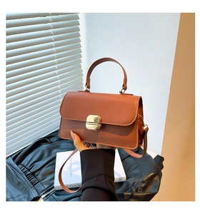 Detail of caramel brown handbag showing glossy gold twist lock and fine PU leather texture