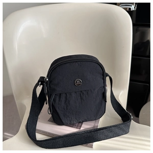 Detail of minimalist black nylon crossbody bag with M FASHION logo on a white chair