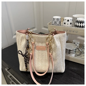Close-up of woven straw tote bag with pink leather strap and gold chain detail