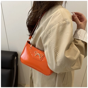 Detail of orange patent leather baguette bag with a silver bow on a beige coat outfit