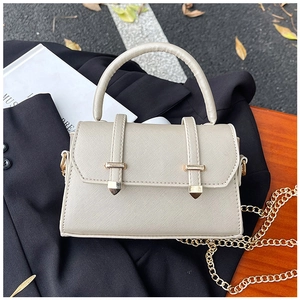 Détail du sac en cuir crème avec chaîne dorée et poignée sur un fond sombre élégant