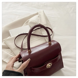 Detail of hand holding a deep red leather handbag with a gold twist lock closure
