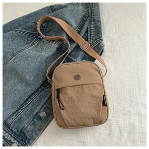 Macro detail of khaki nylon crossbody bag showing the metallic M logo and texture