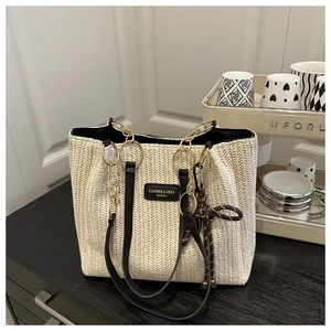 Close-up of woven straw tote bag with gold chain handles and black leather strap detail