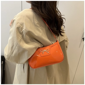 Orange patent leather baguette bag with silver bow accent worn as an underarm shoulder bag