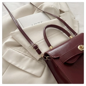Detail of burgundy leather handbag with gold hardware worn over a beige blazer