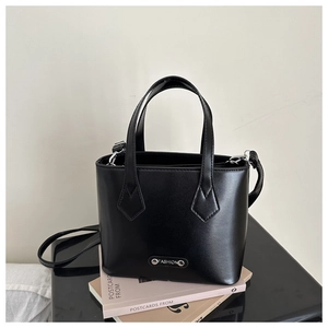 Detailed macro view of black minimalist bucket bag with metal 'FASHION' tag and strap
