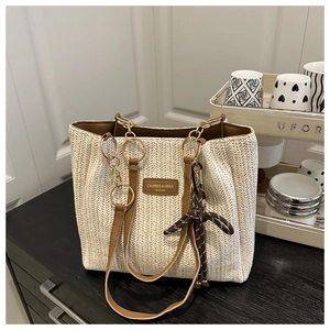 Detail of straw woven tote bag with brown leather brand tag and metal hardware
