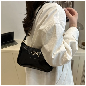 Detail of black glossy patent leather shoulder bag with gold metal bow buckle