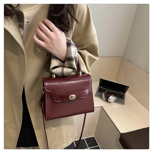 Close-up of a burgundy leather handbag with a gold twist lock and khaki coat background