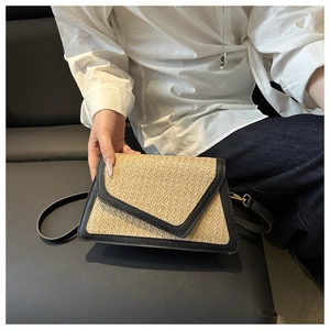 Detail of hand-held woven beige crossbody bag with black leather trim and gold hardware