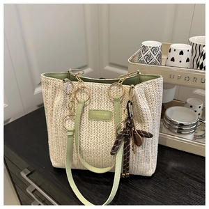 Detail of woven straw tote bag with green leather trim and golden ring hardware