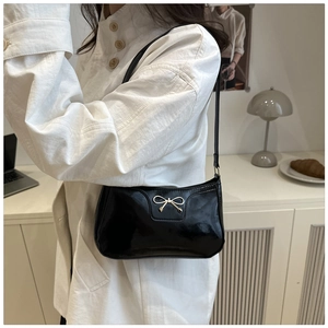 Close-up of a glossy black faux leather baguette bag featuring a gold metal bow buckle