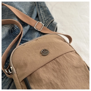 Detailed close-up of khaki nylon handbag featuring M FASHION bronze logo and woven strap
