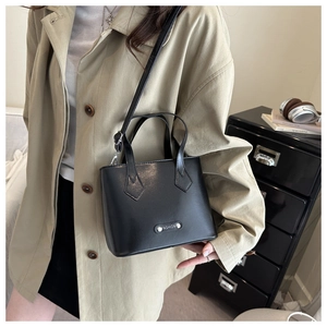 Detailed view of black leather bucket bag worn crossbody with beige trench coat