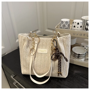 Close-up of woven cream tote bag with gold chain handle and decorative knot charm