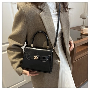 Detail of glossy black patent leather crossbody bag featuring gold twist-lock closure