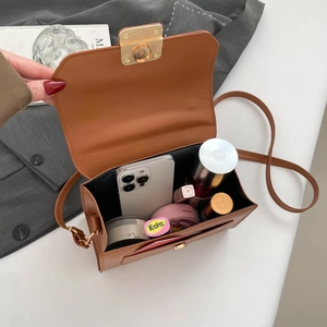 Brown leather crossbody flap bag showing internal capacity with a gold magnetic buckle