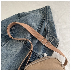 Close-up of khaki nylon crossbody bag with adjustable fabric strap on denim jacket