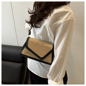 Detailed view of woven straw shoulder bag with black leather trim worn by model