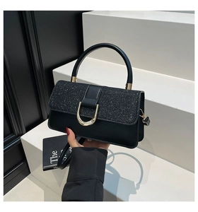 Detail of elegant black faux leather handbag with shimmering glitter flap and gold horseshoe buckle