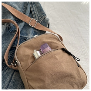Macro detail of khaki nylon crossbody bag featuring front zipper pocket and metal buckle