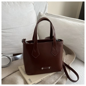 Close-up of a dark brown bucket bag with a metal brand tag on a cozy sofa setting