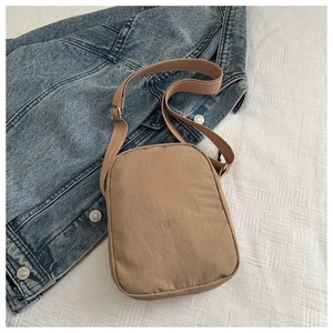 Detail view of khaki crossbody bag on denim jacket featuring adjustable strap and buckle