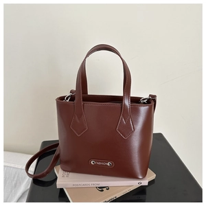 Detailed macro view of dark brown leather bucket bag with metallic FASHION logo plaque